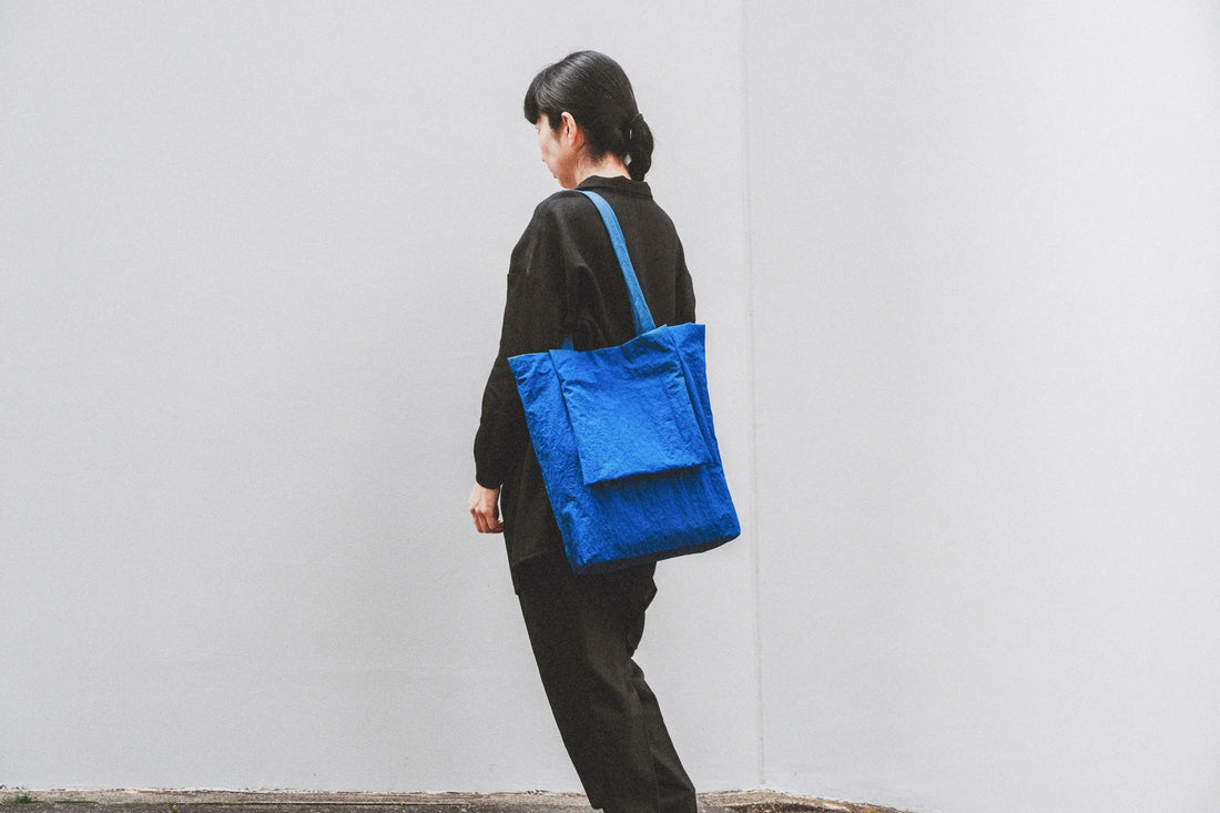 青いformuniform Eco Nylonトートバッグを肩に掛けた人物の後ろ姿